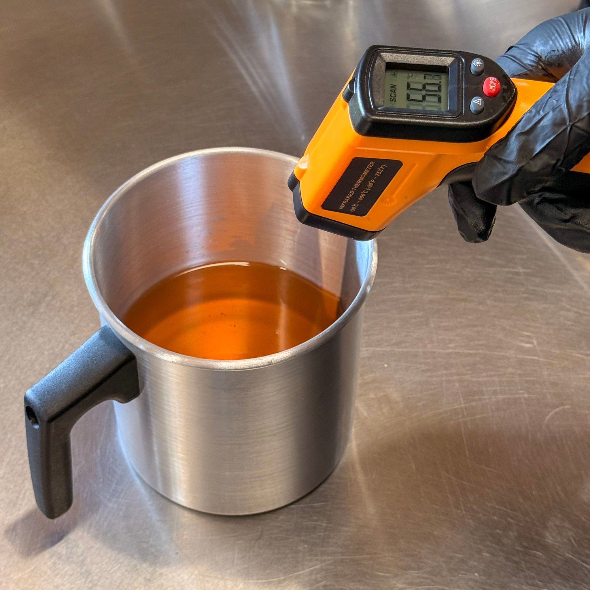 Thermomètre infrarouge numérique mesurant la température de cire fondue orange dans un pot de fusion